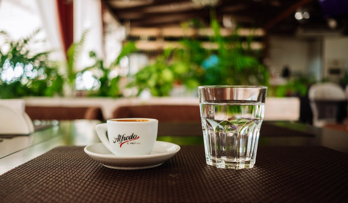 Kaffeetasse und ein Glas Wasser nebeneinander auf einem hellen Küchentisch