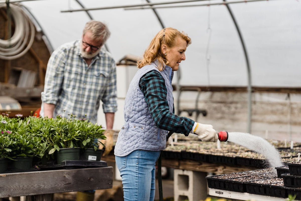 Frau von hinten kniet an einem Hochbeet im Garten und hält eine Handvoll Erde