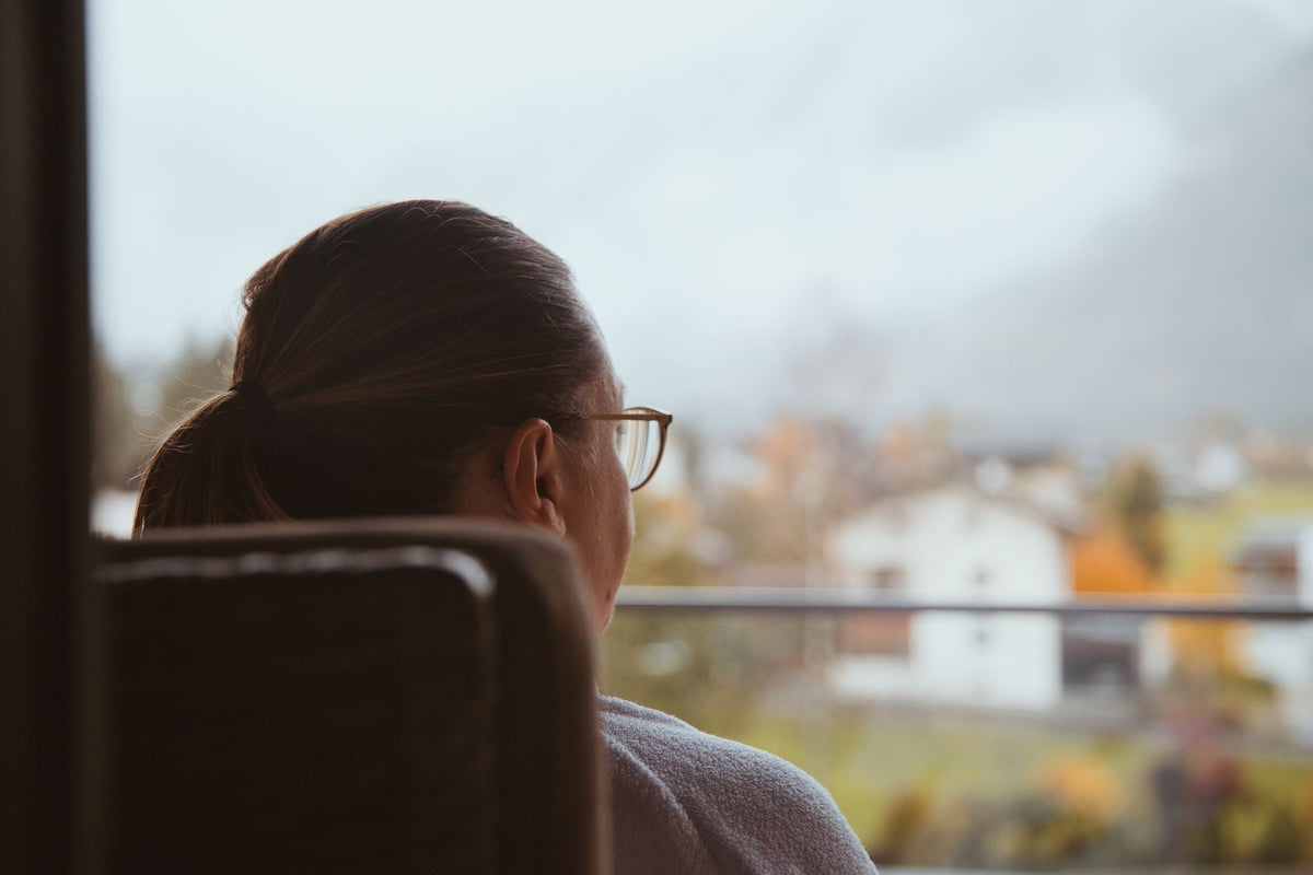 Frau von hinten am Fenster in der Dämmerung, Blick nach draußen